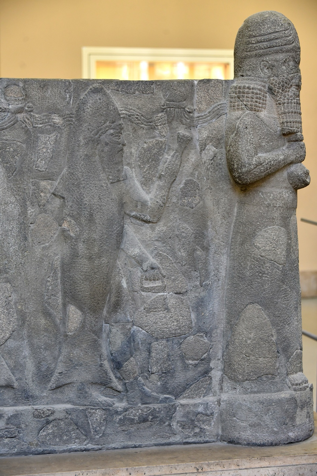 Basalt relief on the side of a large basin: a robed figure with streams running from his shoulders, a figure beside him wearing a fish's head and skin as a cloak, and at the corner a bearded figure carved in the round with a tall headdress.