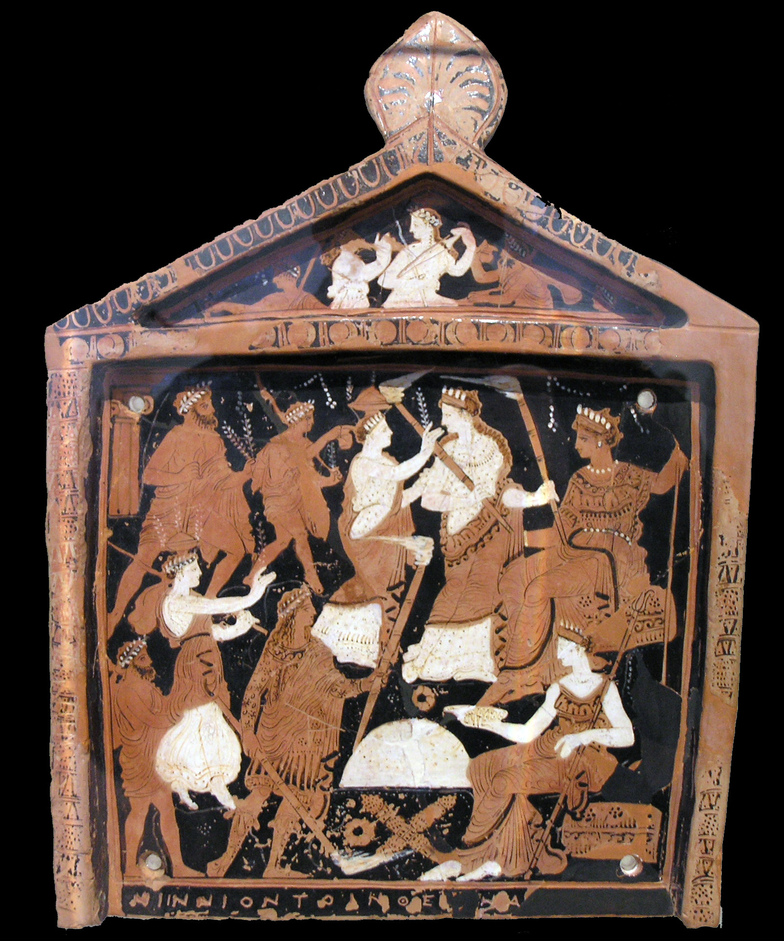 Red-figure clay votive plaque with a pedimented top, painted with two registers of robed figures in procession toward enthroned goddesses, some carrying bundled branches and round-topped vessels, with a Greek dedication inscription along the bottom edge.