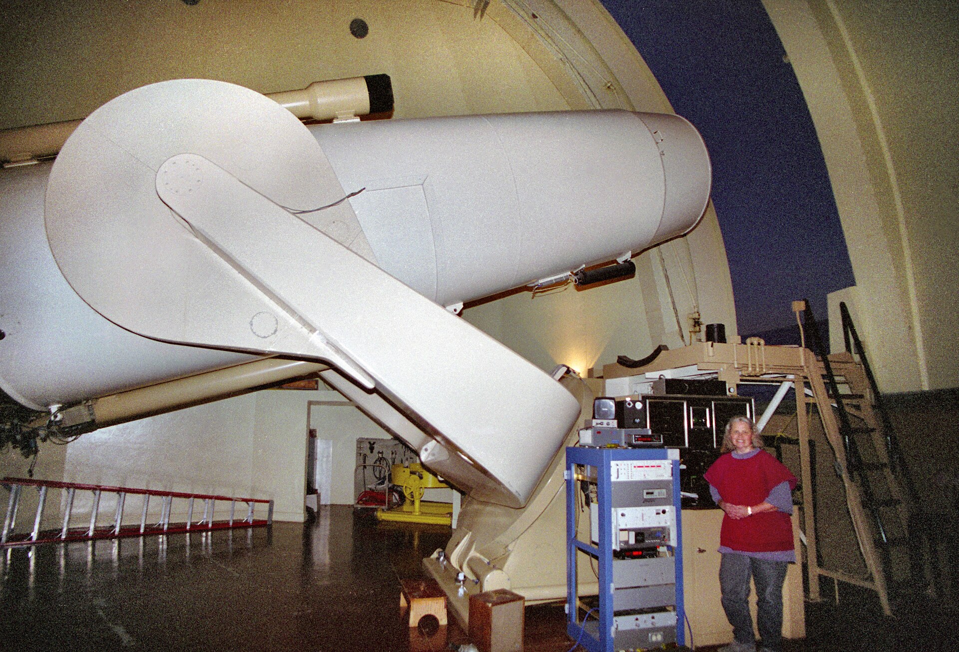 An astronomer stands beside the large white tube of the 48-inch Oschin Schmidt telescope inside its dome at Palomar Observatory.