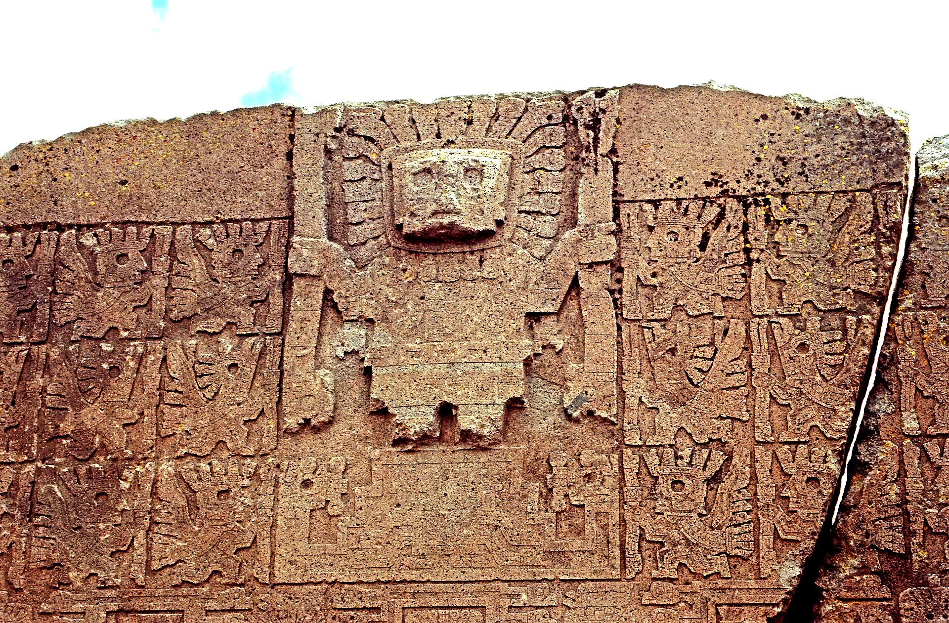 Carved andesite lintel: a central frontal figure with a rayed head holds a staff in each hand, flanked by rows of smaller winged attendants