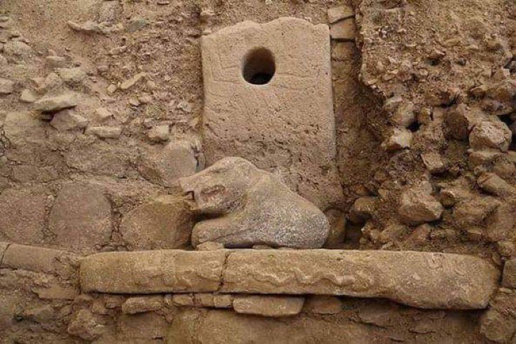 Crouched stone animal in an excavated structure with a perforated slab behind it