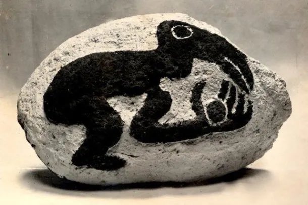 Bird-headed figure with a bent limb near a small rounded object, outlined by dark markings
